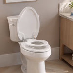 A white family toilet seat in a bathroom setting, showing the topseat built-in child potty training ring lowered and ready for use, with the adult seat and cover raised.