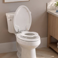 A white family toilet seat in a bathroom setting, showing the topseat built-in child potty training ring lowered and ready for use, with the adult seat and cover raised.